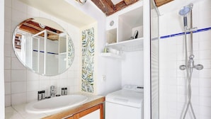 Un bagno con lavandino bianco, uno specchio, doccia con soffione manuale e WC a muro.
