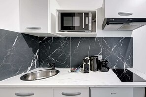 A modern kitchen with a built-in microwave, a stainless steel sink, and a black stovetop. - Elegance et modernite - Parc de la Villette (Paris)