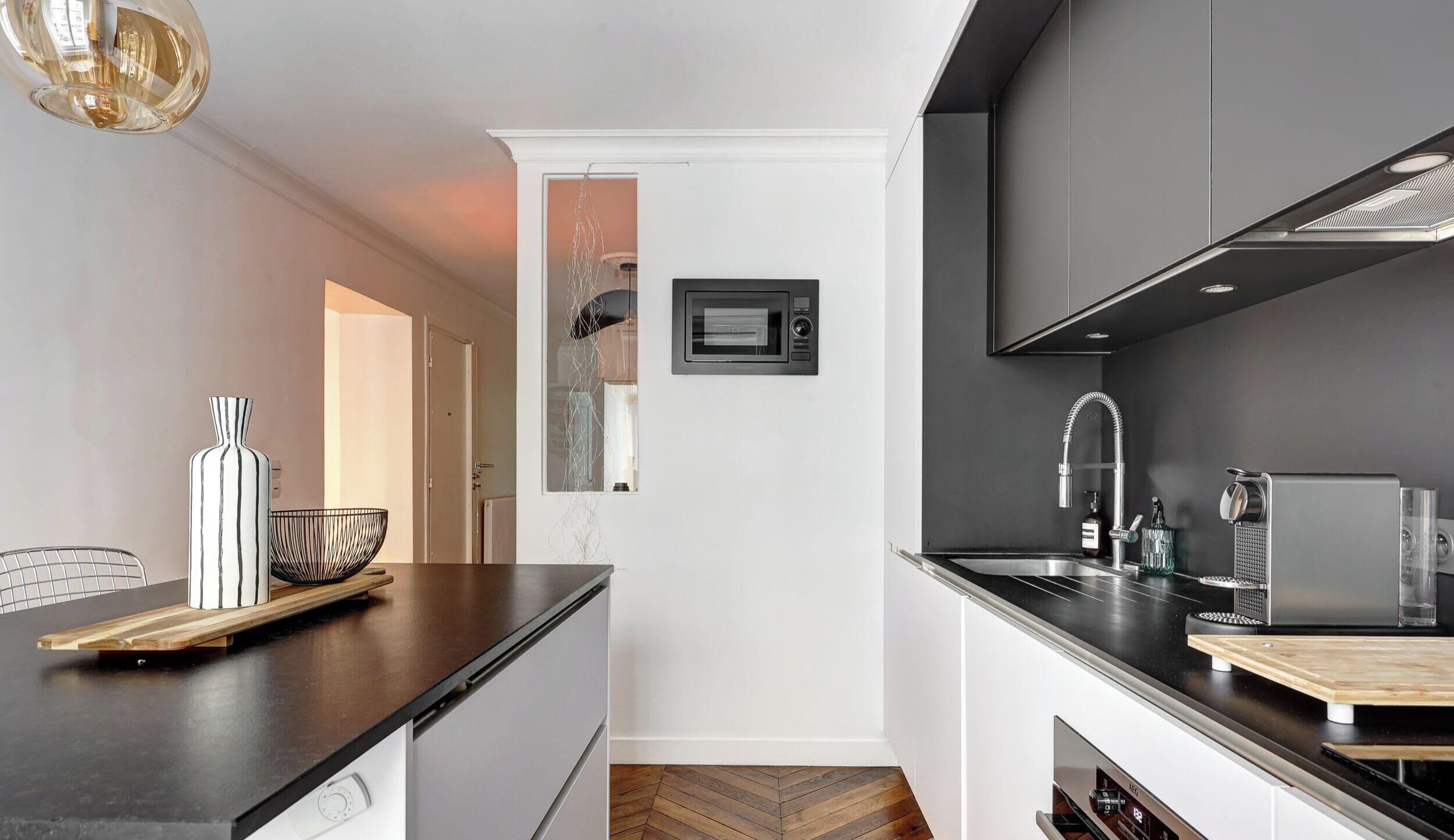A modern kitchen with a black countertop, stainless steel appliances, and a herringbone wood floor.