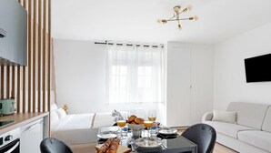 A modern hotel room with a bed, dining table, breakfast setup, and a TV mounted on the wall. - Studio d'Architecte Haut de Gamme - Elegance et Confort - Paris (Paris)