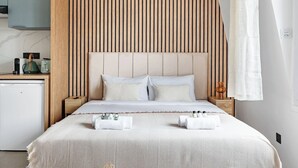 A modern bedroom with a large bed, wooden headboard, bedside tables, and a small kitchenette. - Studio d'Architecte Haut de Gamme - Elegance et Confort - Paris (Paris)