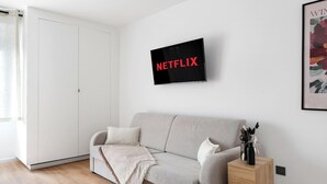 A modern living room with a grey sofa, a white throw blanket, and a black framed sign with "NETFLIX" on it. - Studio d'Architecte Haut de Gamme - Elegance et Confort - Paris (Paris)
