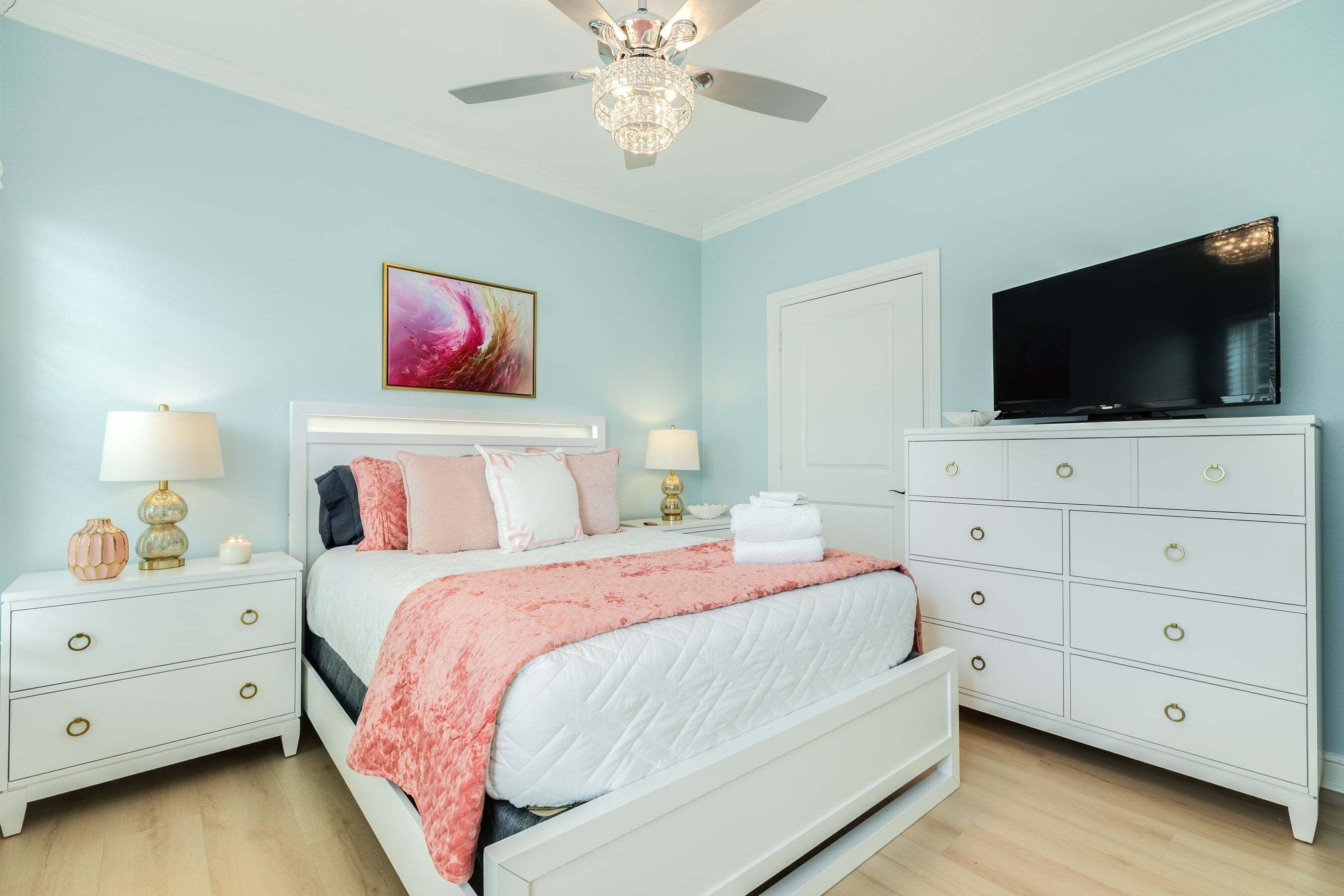 A bedroom with a bed, nightstands, a dresser, a television, and a ceiling fan.