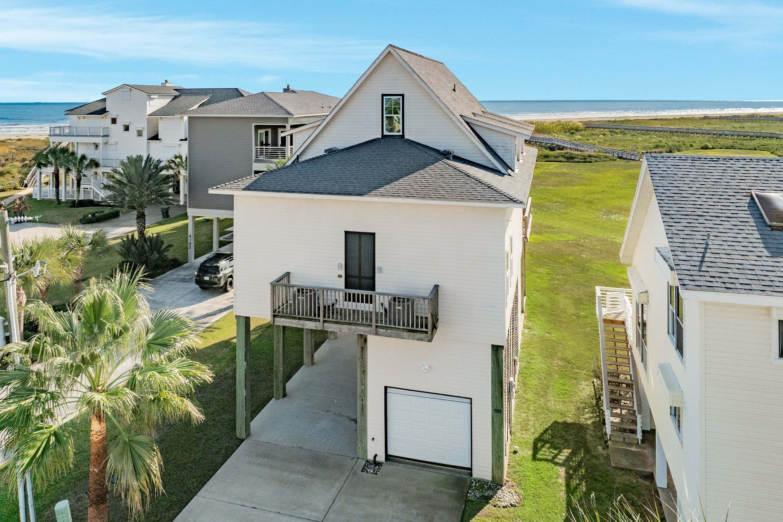 A two-story residential building with a balcony, a garage, and a view of the beach.