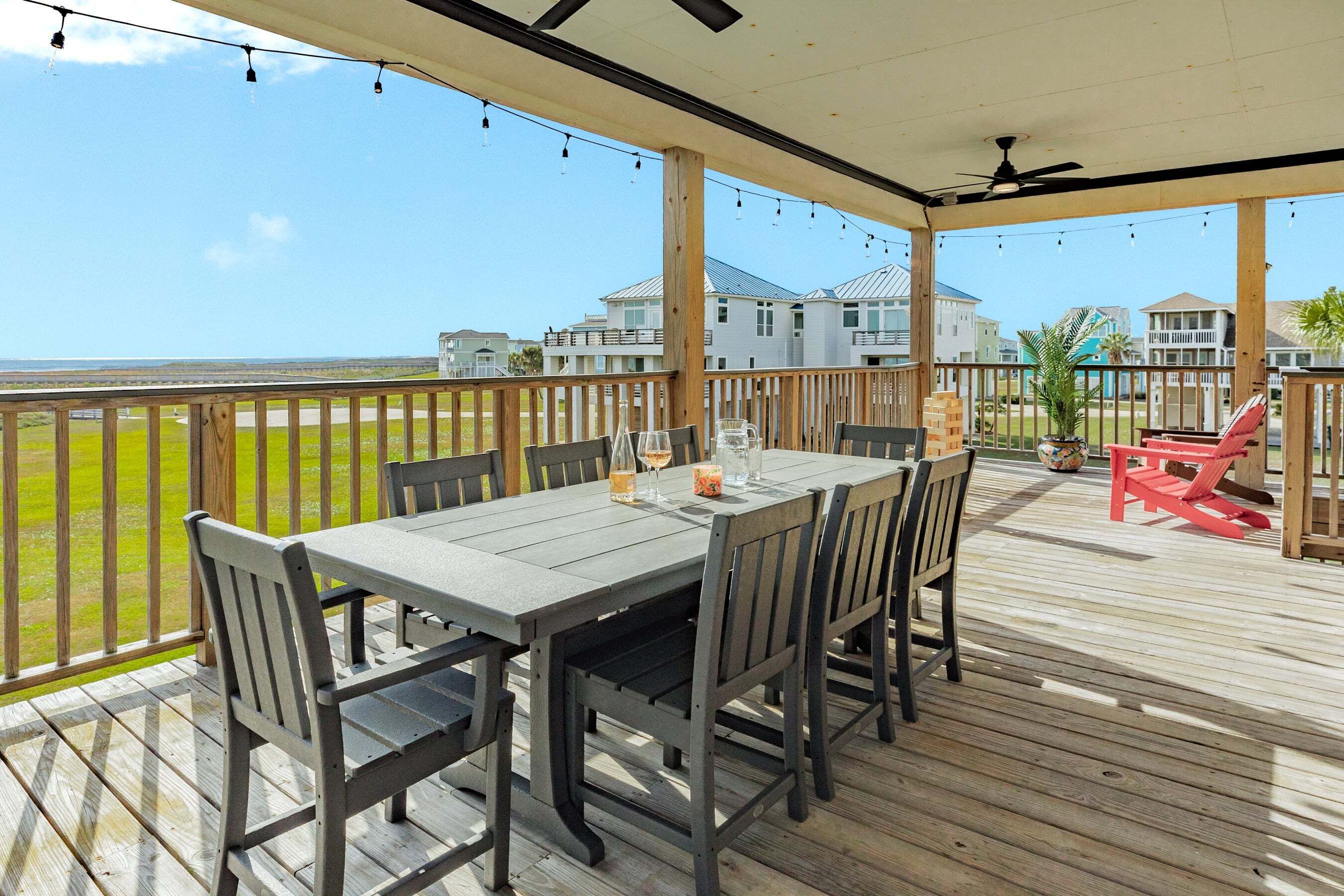 A covered outdoor deck with a table and chairs, overlooking a grassy area and buildings.