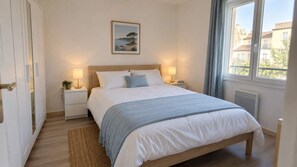 Um quarto com cama, mesas de cabeceira, um criado-mudo, janela com cortinas e um quadro na parede.