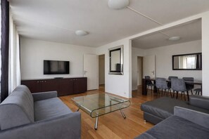 Ein modernes Wohnzimmer mit einem Glastisch, grauen Sofas, einem Flachbildfernseher und einem Essbereich mit Stühlen und einem Tisch.