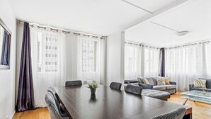 Ein modernes Wohnzimmer mit einem großen dunklen Holztisch, grauen Sofas und transparenten Vorhängen.