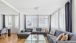 Ein modernes Wohnzimmer mit einem Ecksofa, einem Glastisch und einem Essbereich mit Stuhl und Tisch.
