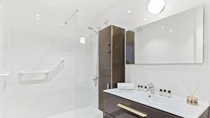 Ein modernes Badezimmer mit Duschkabine aus Glas, einem weißen Waschbecken mit Toilettenartikeln und einem großen Spiegel.