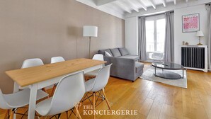 A modern living room with a wooden dining table, white chairs, a grey sofa, and a round coffee table. - Magnifique duplex avec terrasse et vue imprenable sur la Tour Eiffel (Paris)