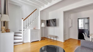 A modern living room with a wooden staircase, a flat-screen TV mounted on the wall, and a grey sofa. - Magnifique duplex avec terrasse et vue imprenable sur la Tour Eiffel (Paris)