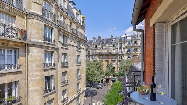 A narrow street between buildings with balconies, a small table with a bottle and glass, and a car parked on the street. - Magnifique duplex avec terrasse et vue imprenable sur la Tour Eiffel (Paris)