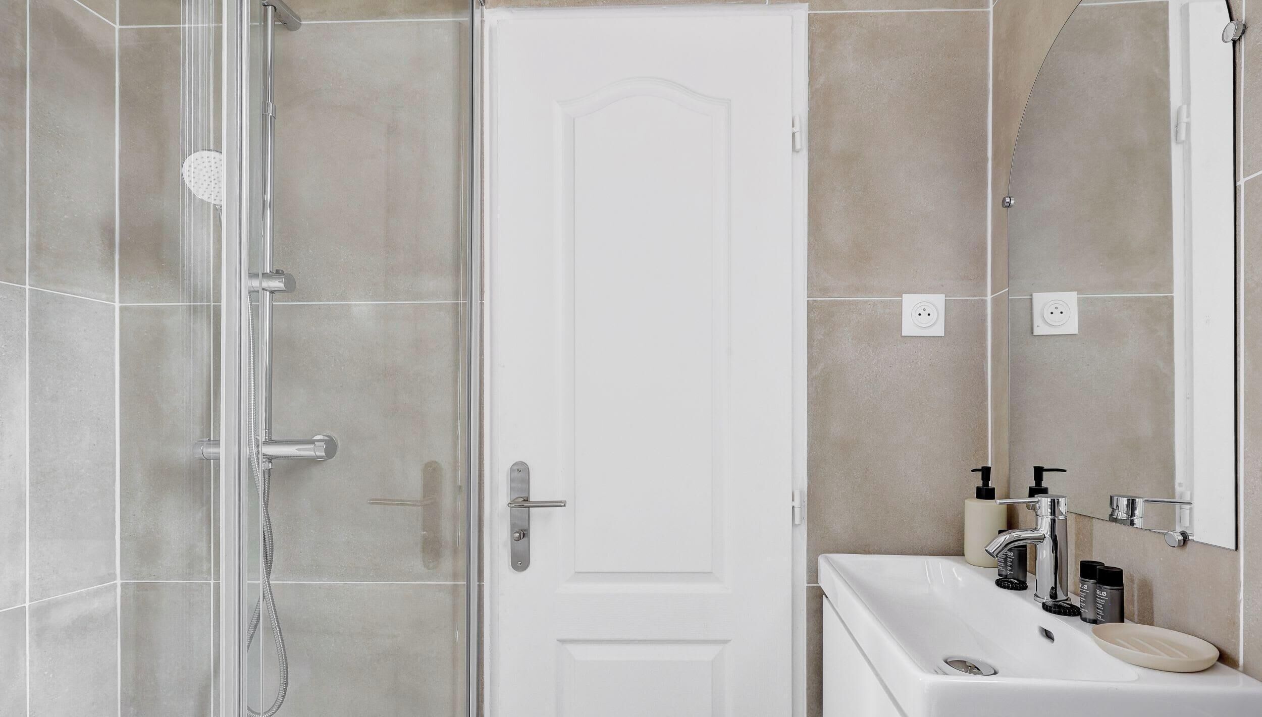 Een moderne badkamer met een douchecabine van glas, een witte deur en een wastafel met toiletartikelen.