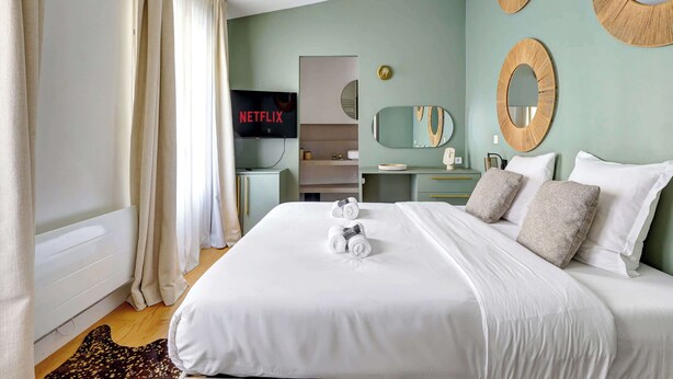 Una camera d'albergo con un letto grande, una televisione che mostra 'NETFLIX', uno specchio e una parete con specchi circolari.