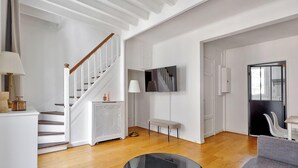Ein modernes Wohnzimmer mit einer Holztreppe, einem an der Wand montierten Flachbildfernseher und einem grauen Sofa.