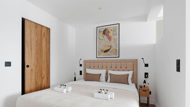 Una cama bien hecha con cabecera, una puerta de madera y una obra de arte enmarcada encima.