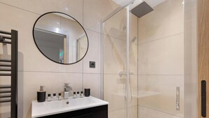 Un baño moderno con un lavabo blanco, un espejo redondo y una ducha con paredes de vidrio.