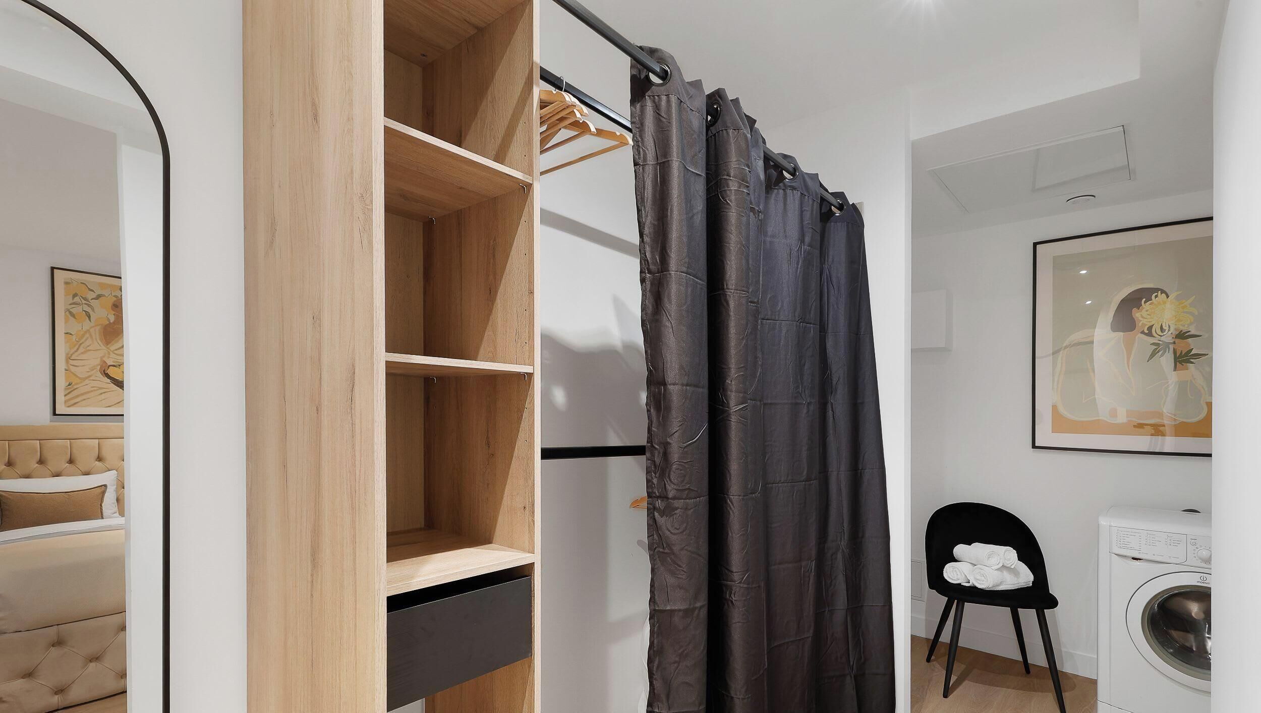 Un baño moderno con tocador de madera, cortina de ducha negra, lavadora y un cuadro en la pared.