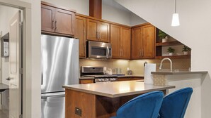 A compact kitchen with wooden cabinets, stainless steel appliances, and a small island with blue chairs.