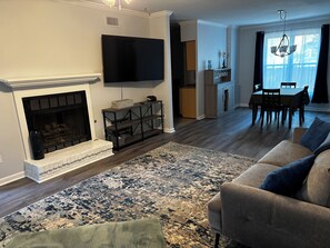 A living room with a fireplace, a flat-screen TV, a dining area with a table and chairs, and a kitchen in the background. - 3-bedroom condo in Augusta 4mi from Augusta National (Augusta)