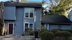 Une maison à deux étages avec une porte rouge, une cheminée et une boîte aux lettres.