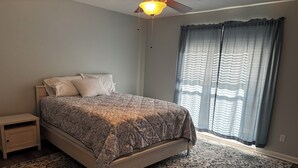 Une chambre à coucher avec un lit, une table de chevet et une grande fenêtre avec des rideaux.