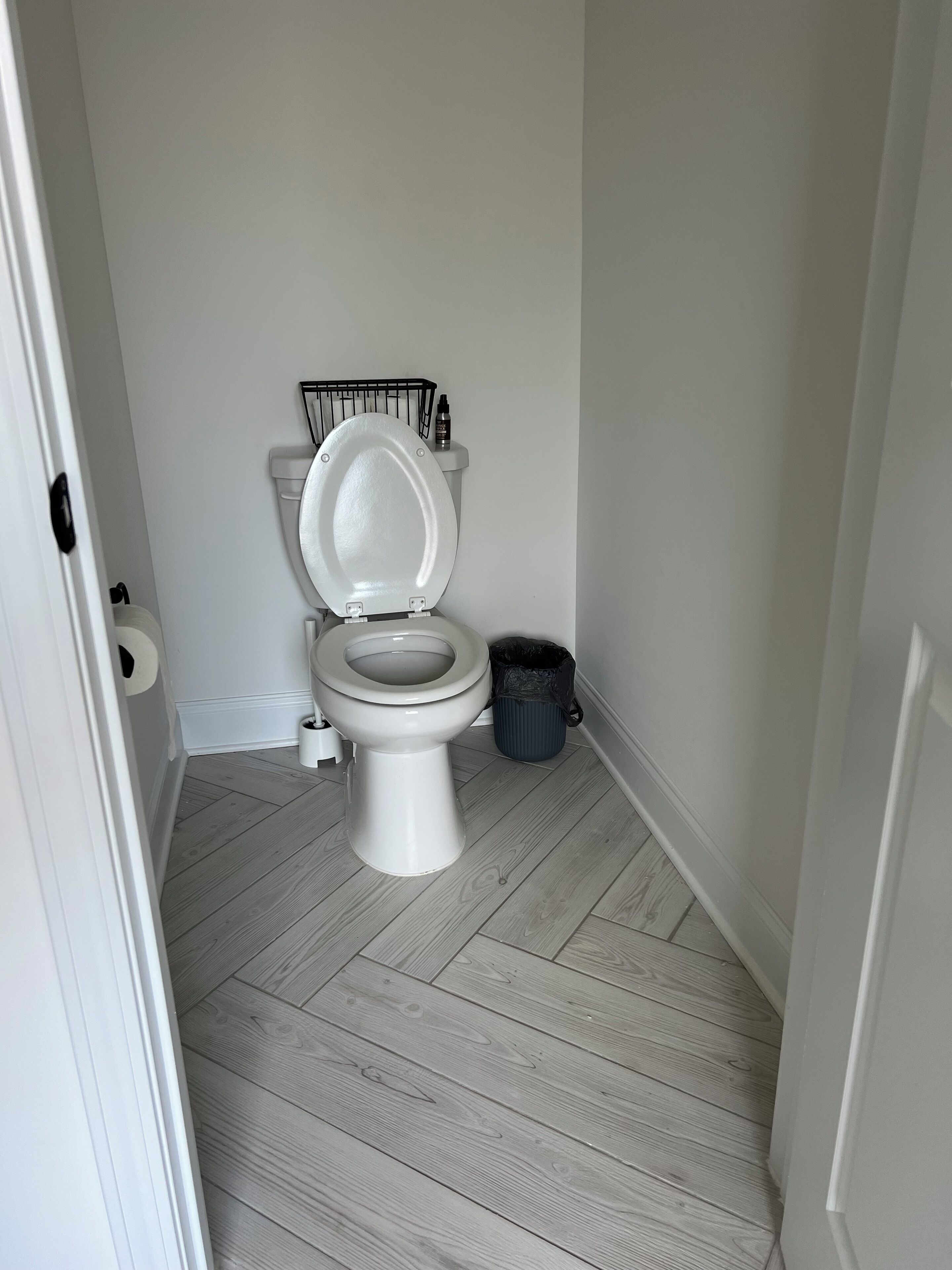 Un baño pequeño y limpio con inodoro blanco, un cubo de basura negro y una puerta blanca.