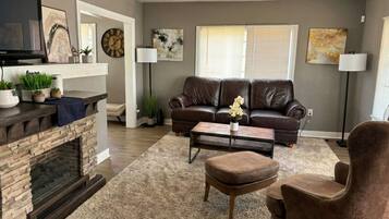 A living room with a fireplace, leather sofa, coffee table, and a TV.