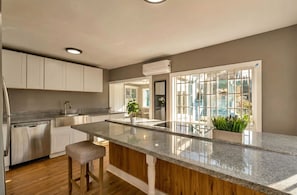 A modern kitchen with a central island, stainless steel appliances, and a view through a large window.