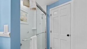 A bathroom with a glass shower enclosure, a white door, and a towel rack. - Newly Remodeled Cape Home in Hyannis – Sleeps 10 Comfortably (Barnstable)