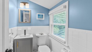 A bathroom with a toilet, sink, cabinet, and window with blinds. - Newly Remodeled Cape Home in Hyannis – Sleeps 10 Comfortably (Barnstable)