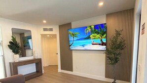 En moderne stue med et fladskærms-tv, en sofa, et lille bord og en potteplante.