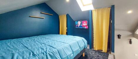 Un dormitorio con cama, televisor, tragaluz y puerta con cortinas.