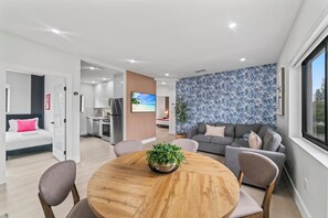 Een moderne woonkamer met een ronde houten tafel, een grijze bank en een televisie bevestigd aan een muur met tropische behang.