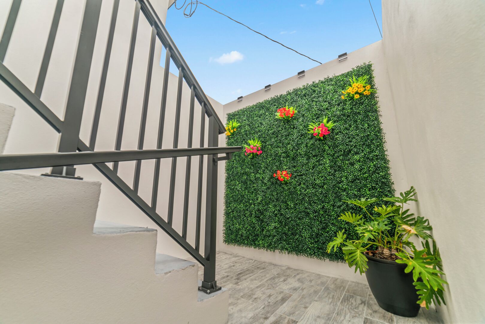 A staircase with a metal railing, a wall with green foliage and flowers, and a potted plant.