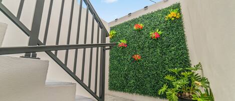 A staircase with a metal railing, a wall with green foliage and flowers, and a potted plant.
