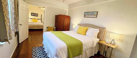 Une chambre à coucher comprenant un lit, un ventilateur de plafond, une armoire en bois, une table de chevet avec une lampe et un tapis à motifs.