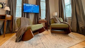 Una habitación acogedora con dos sillones reclinables verdes, techo de madera, televisión de pantalla plana y una ventana con cortinas.