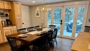 Un comedor con mesa y sillas de madera, una cocina con armarios de madera y vistas a través de puertas de cristal.