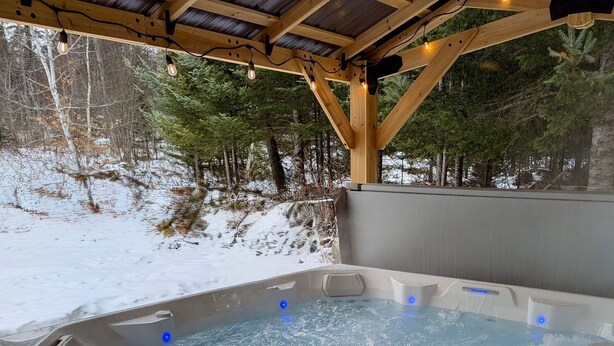 Un jacuzzi con una pérgola de madera encima, rodeado por un paisaje nevado y árboles.