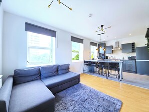 Un appartement moderne avec un canapé gris, une cuisine dotée d’un îlot central et un coin repas avec des tabourets de bar.