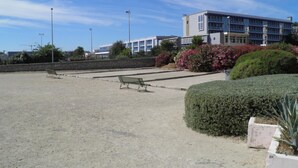 Un espacio al aire libre con un banco, un sendero pavimentado y un edificio al fondo.