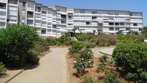 Un edificio residencial de varios pisos con balcones, rodeado de jardines ajardinados y un sendero pavimentado.