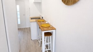 Una cucina compatta con un piano di lavoro in legno, due sgabelli, un armadietto bianco e uno specchio fissato alla parete.