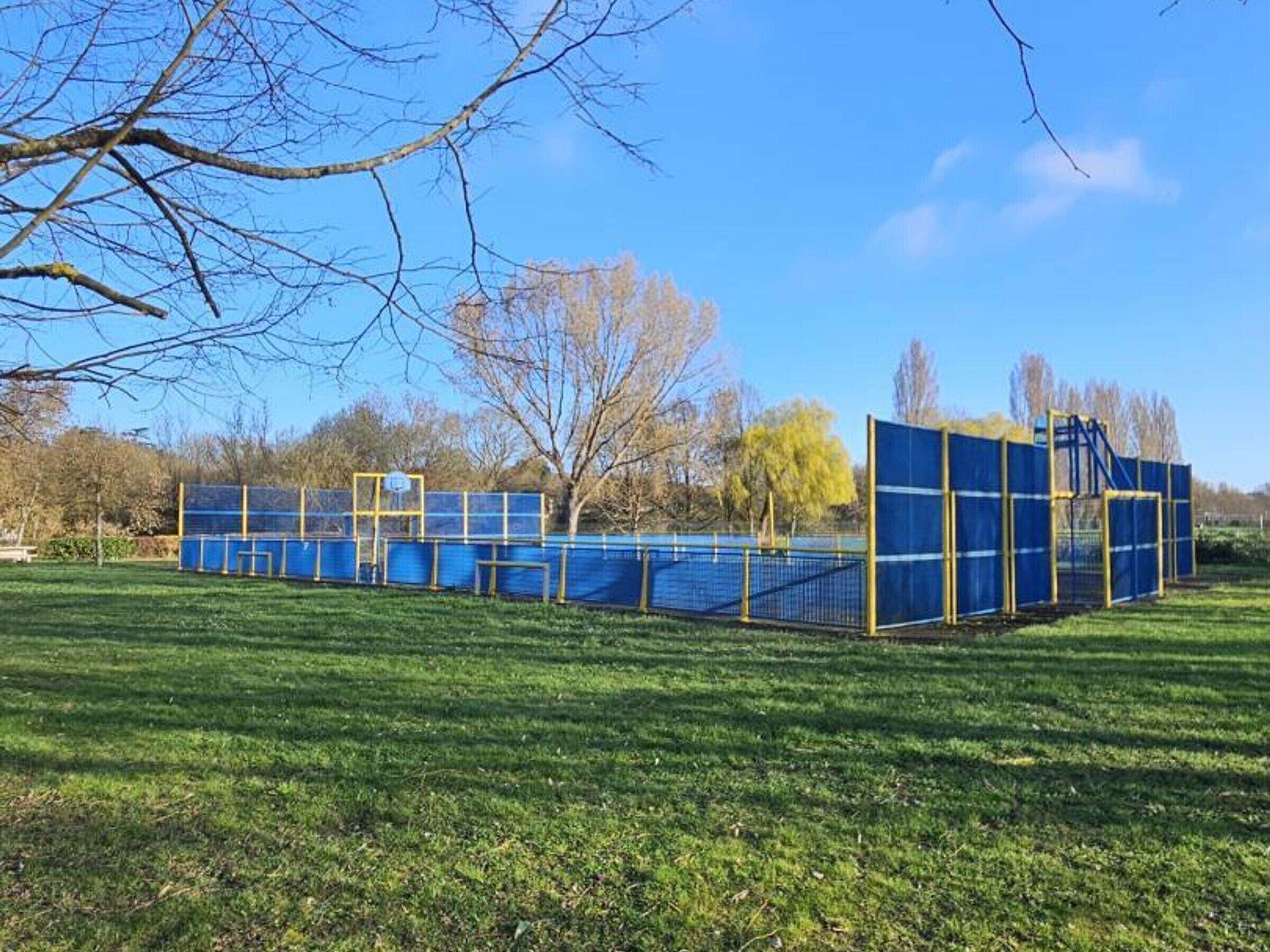 Un campo deportivo cercado con un poste de portería y una estructura azul con red.