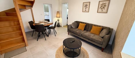 A modern living room with a wooden staircase, a dining area, a sofa with cushions, and a coffee table.