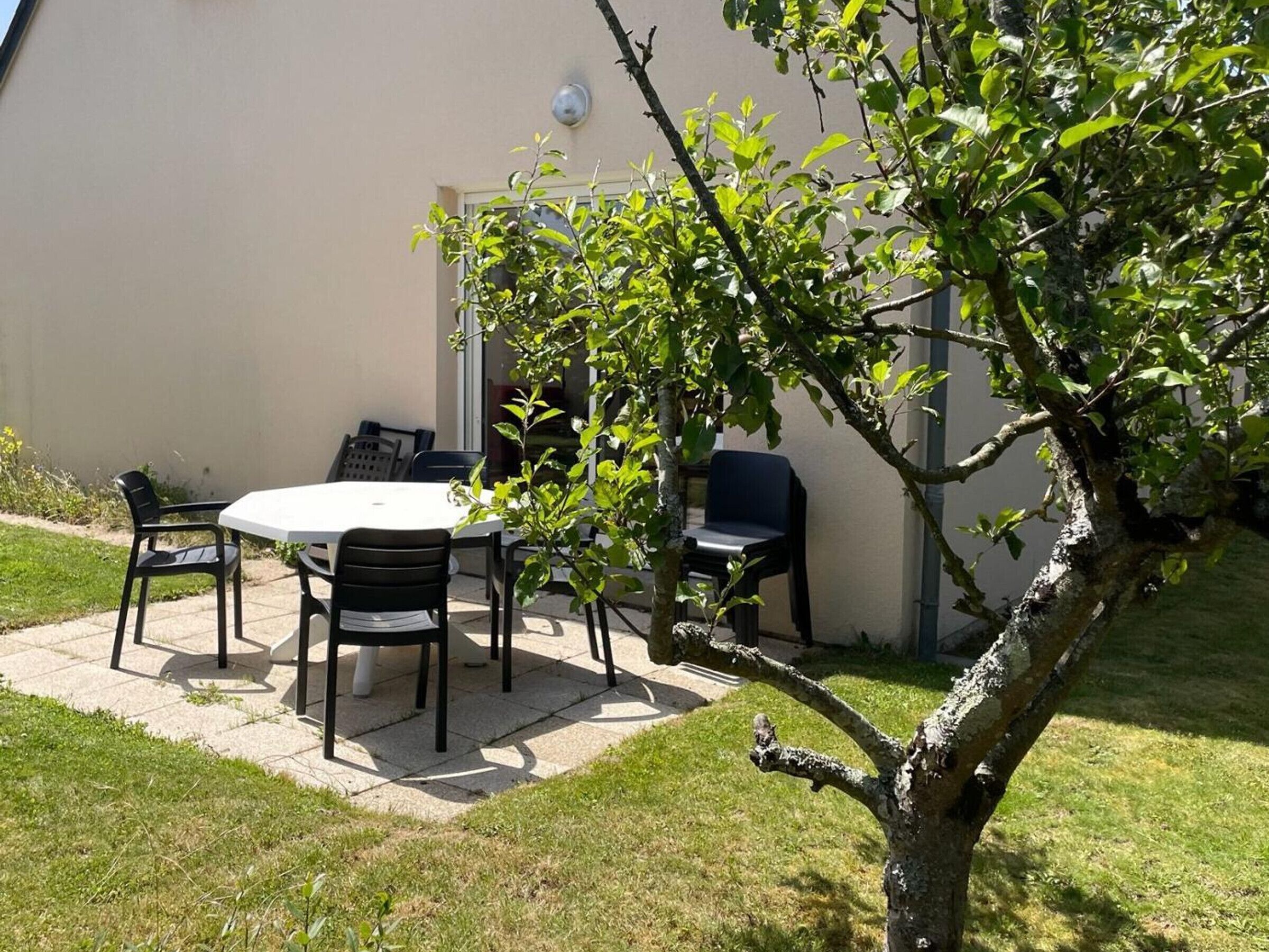 Een terras buiten met een tafel, stoelen, een kleine boom en een gebouw op de achtergrond.