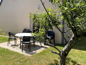 An outdoor patio with a table and chairs, a small tree, and a building in the background. - Spacious house, pets welcome - 5 guests (La Feuillie)