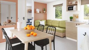 A modern living space with a dining area, a green sofa, and a kitchen area with a microwave. - Spacious mobile home - 8 guests (Visan)